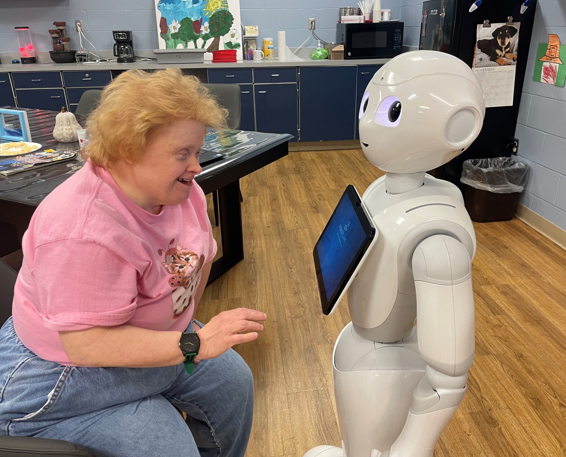 Smiling woman in pink shirt looks at touch screen on a humanoid robot.