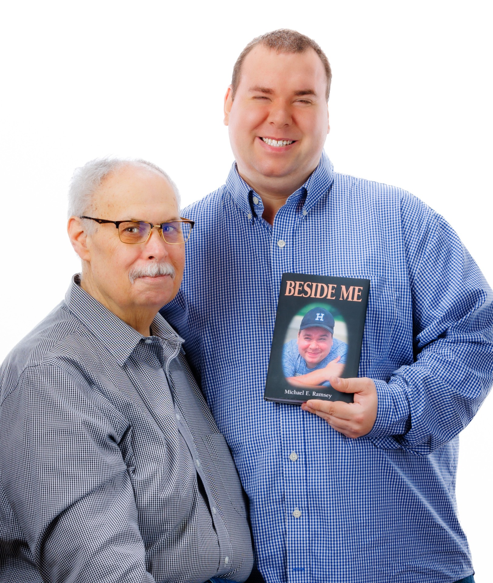 Father and adult son smiling with a copy of their book